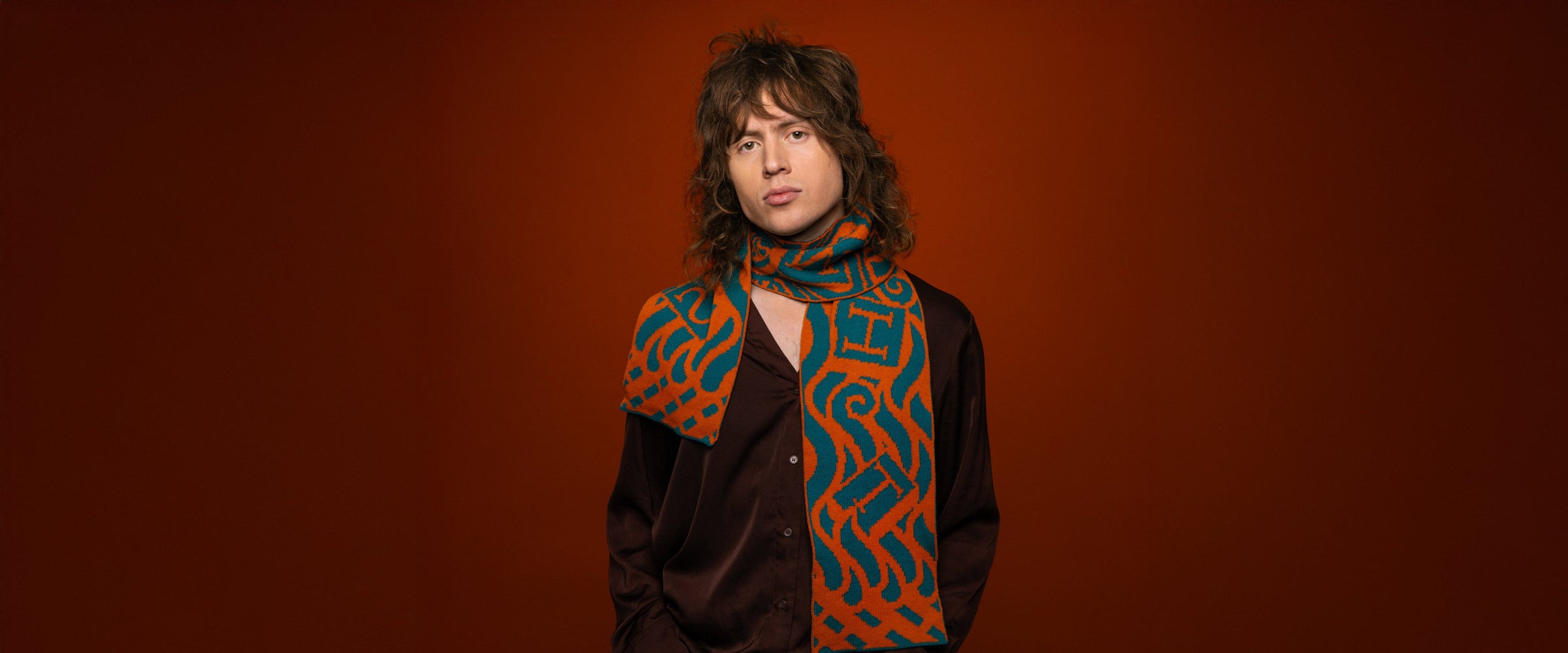 Model wearing a merino-cashmere blend knitted scarf in orange and teal