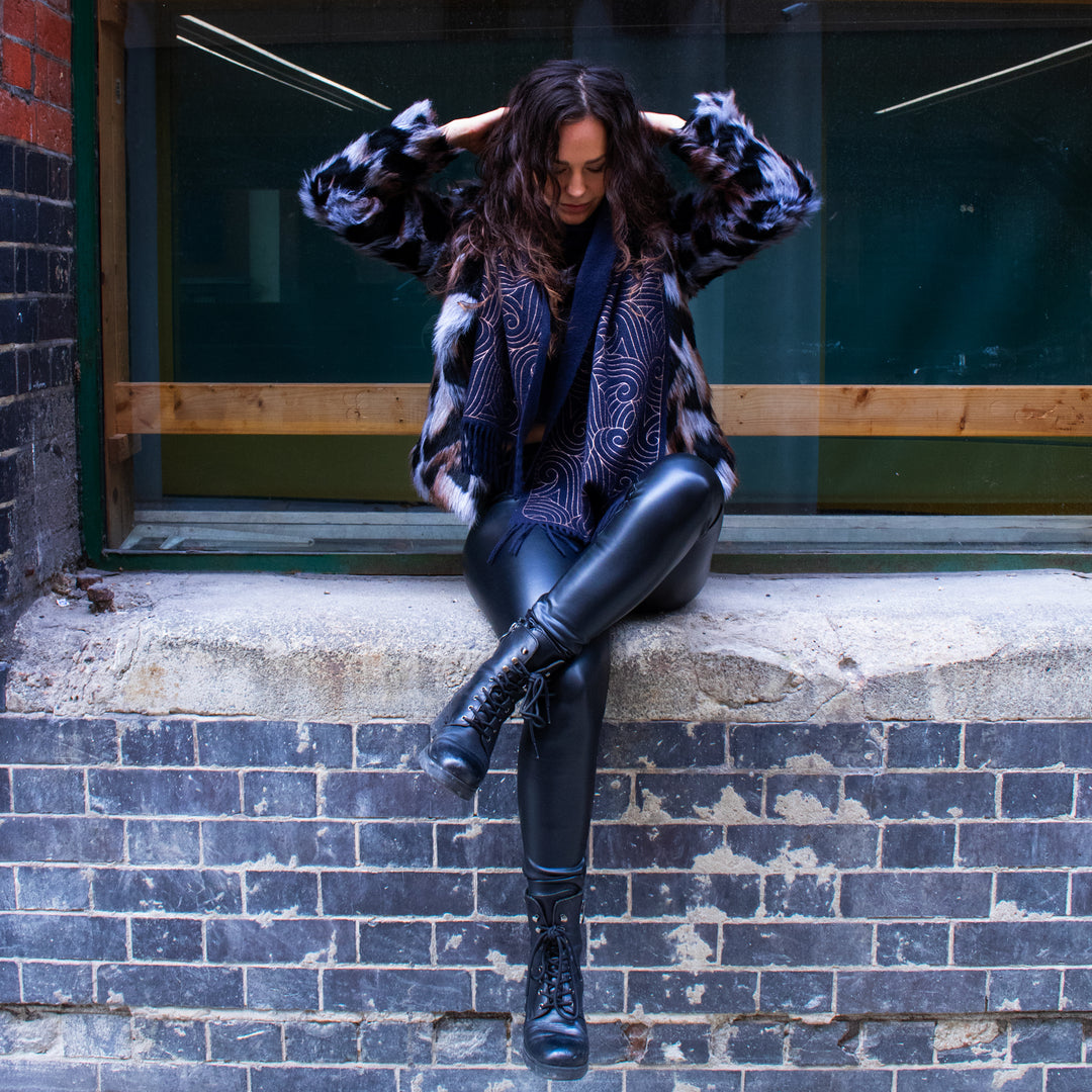 Woman sitting on a brick step wearing a patterned coat and black leather pants and a Furious Goose cashmere scarf in navy and copper | Made in England