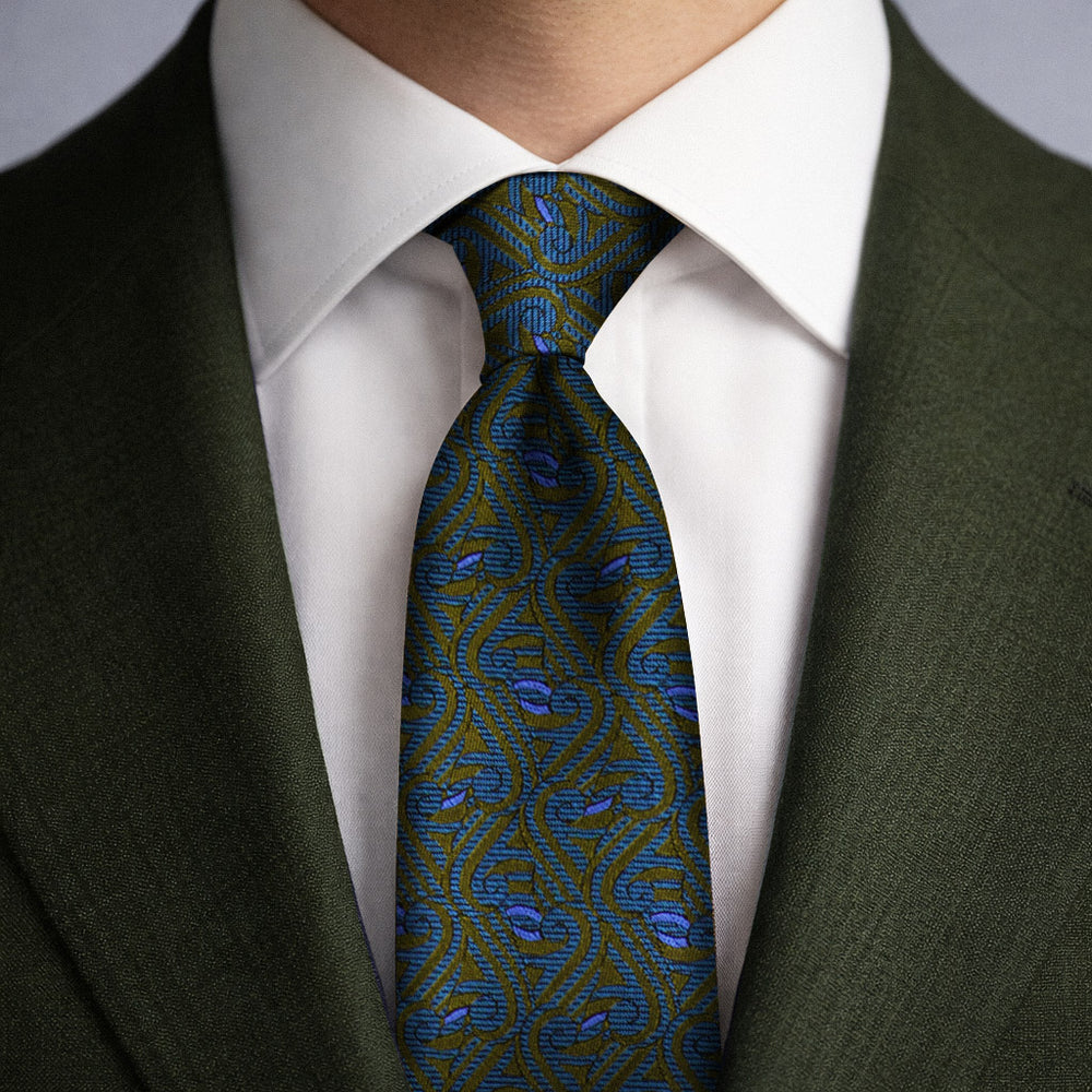 A olive green, teal and blue silk woven tie shown with a green blazer